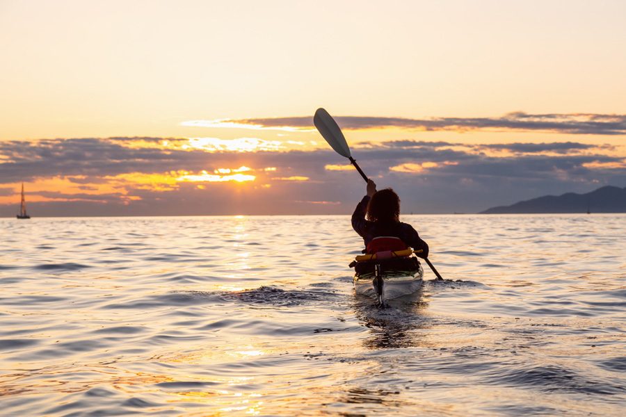 Girl sea kayaking during a vibrant sunny summer sunset